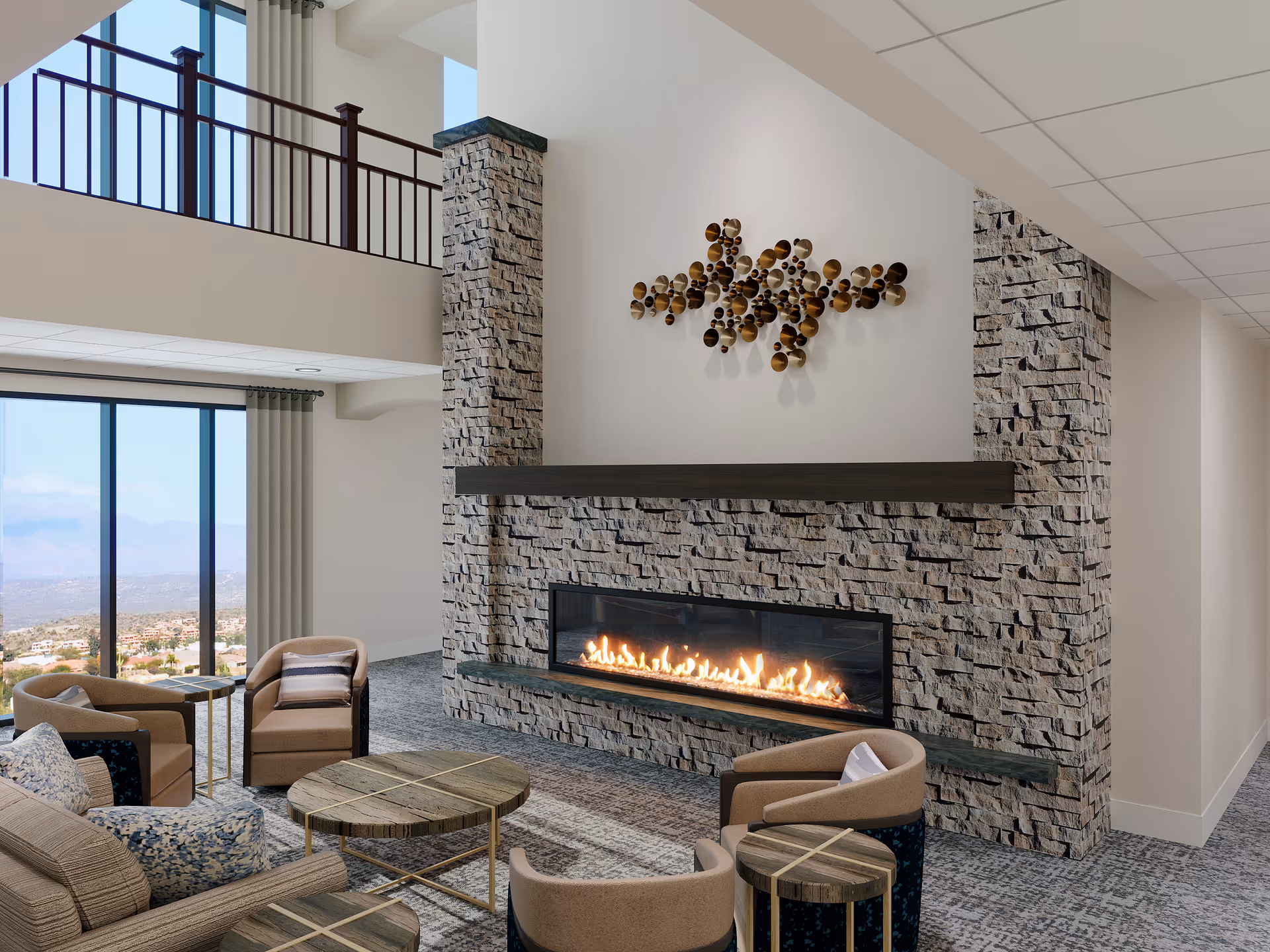 Communal lounge with chairs and tables facing a long modern fireplace set in a stone wall and large windows with a view.