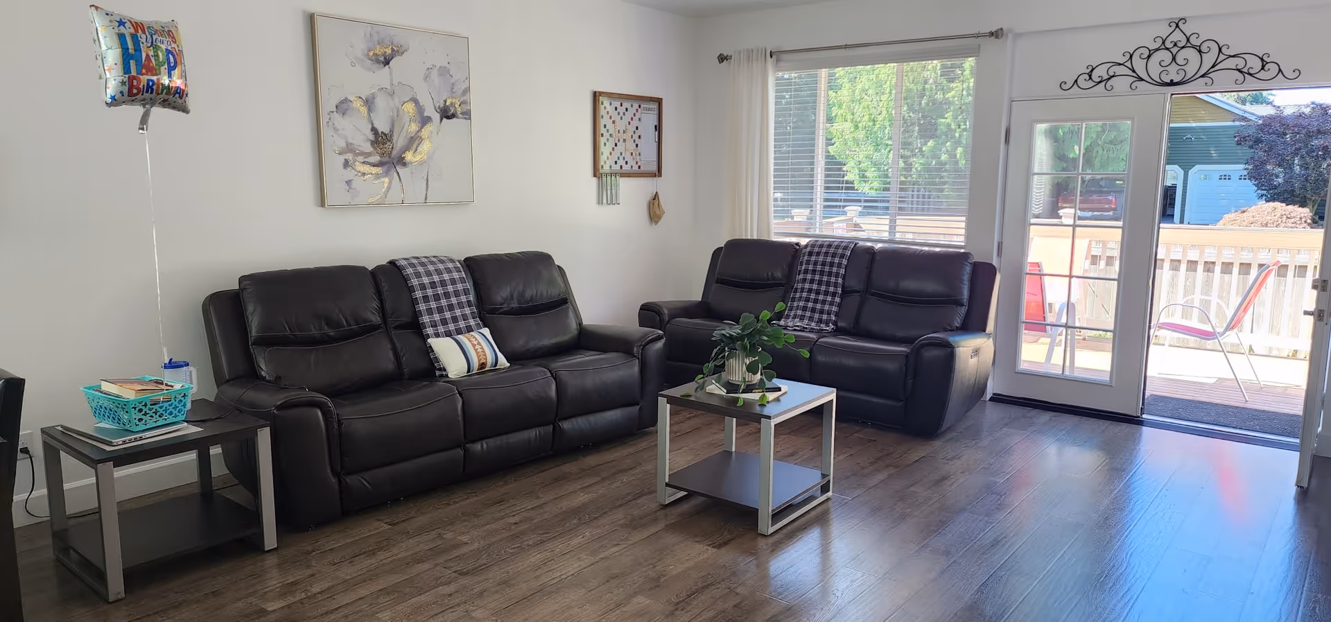 Cozy living room with black leather sofas, coffee table, wall art, and a sunny outdoor patio.