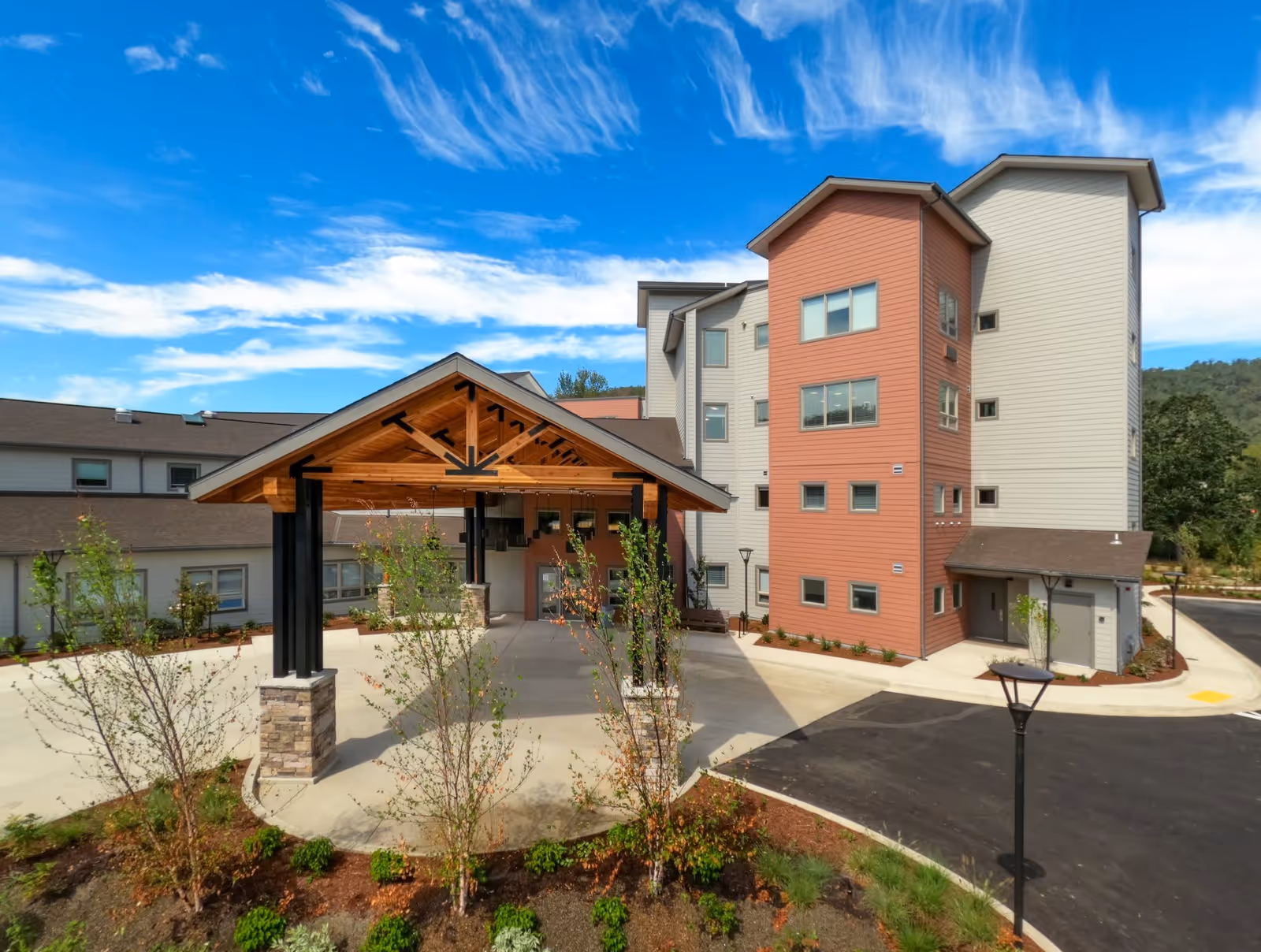 Exterior view of The Landing a Senior Living Community building with a covered entrance supported by stone and black pillars, surrounded by landscaped greenery and a clear blue sky with scattered clouds.