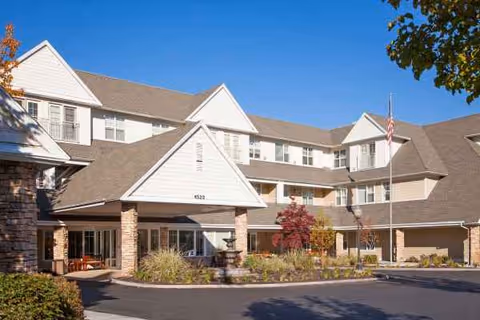 Front view of The Wellington senior living facility with entry, landscaping, and flag.