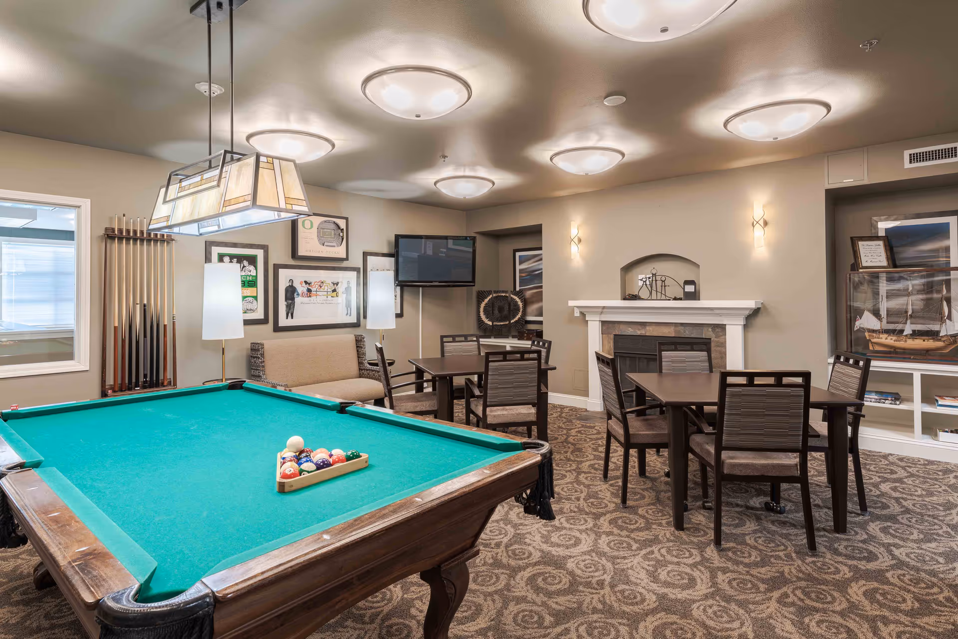A community game room featuring a pool table with racked balls, seating and dining tables, a fireplace, and a wall-mounted TV.