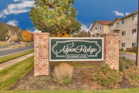 Aspen Ridge Retirement Living sign on brick pillars with landscaping.