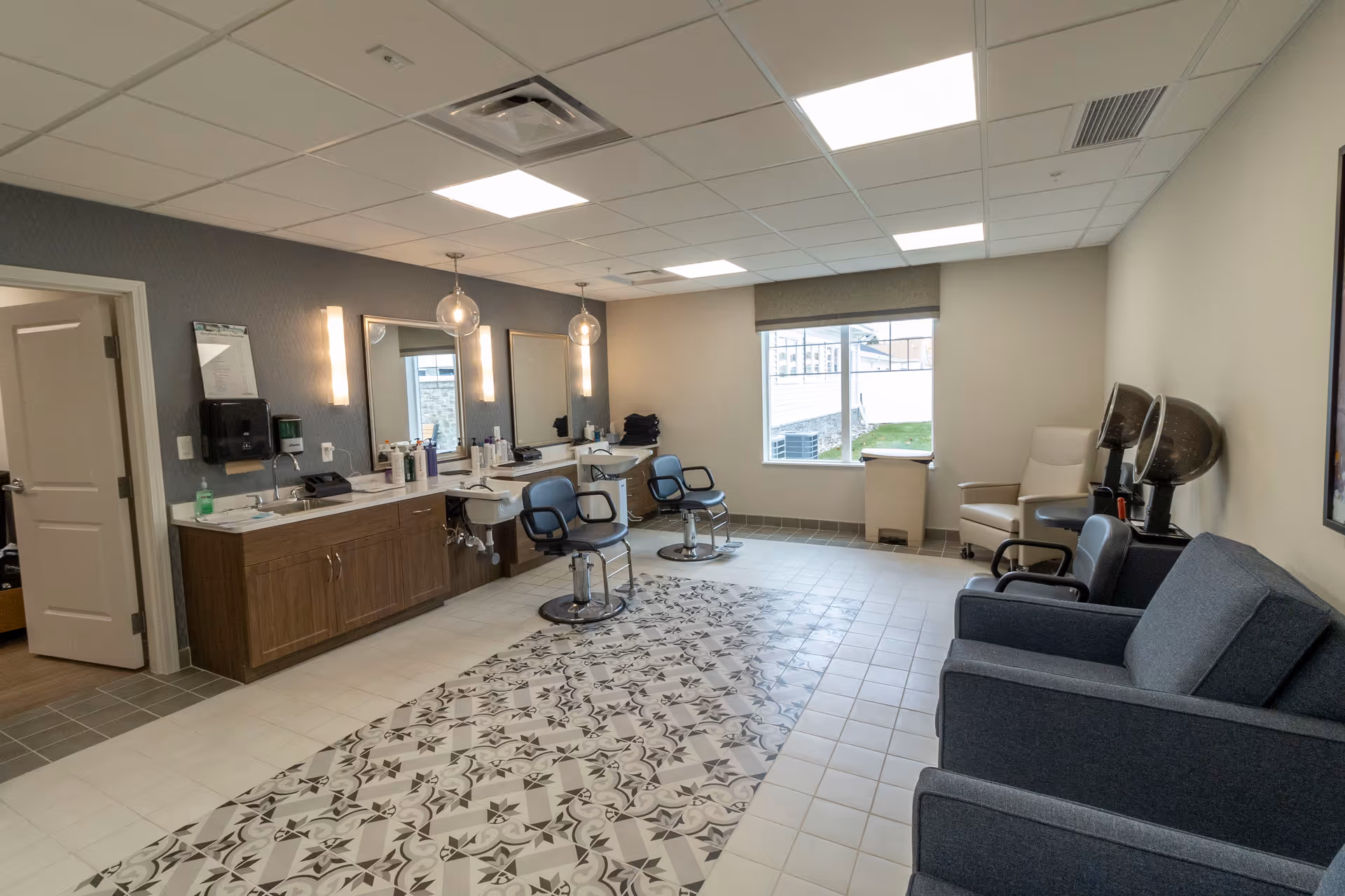Interior salon room with barber chairs, sinks, mirrors, seating and a decorative tiled floor.
