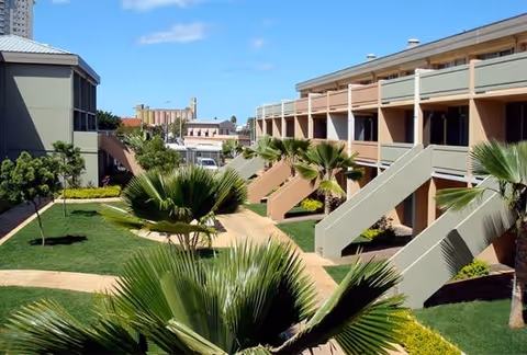 Two-story Kukui Gardens building with exterior staircases, balconies, and palm-lined landscaped walkways.