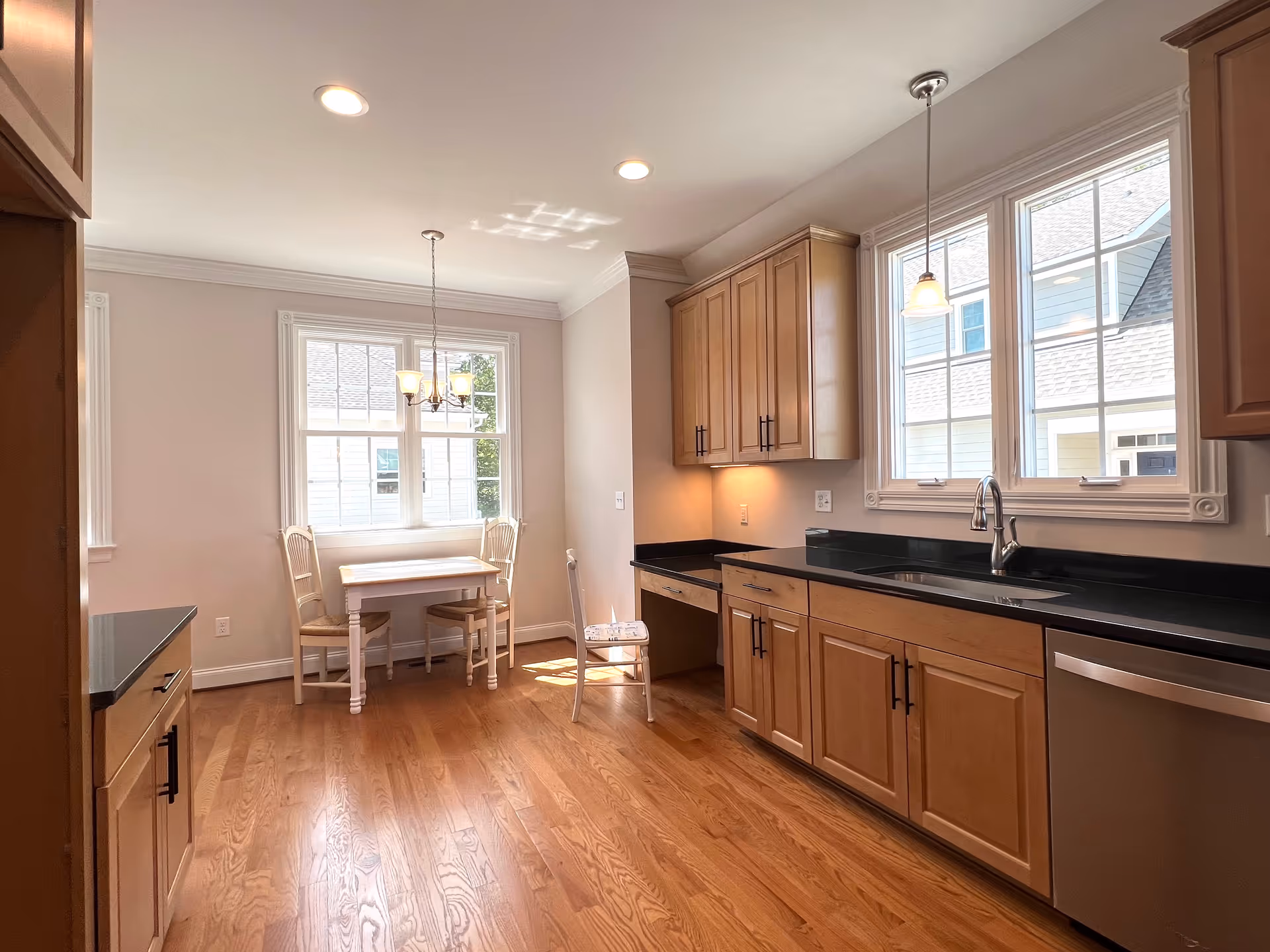 Bright kitchen with wood cabinets, black countertops, a stainless sink and dishwasher, and a small dining nook by the window.