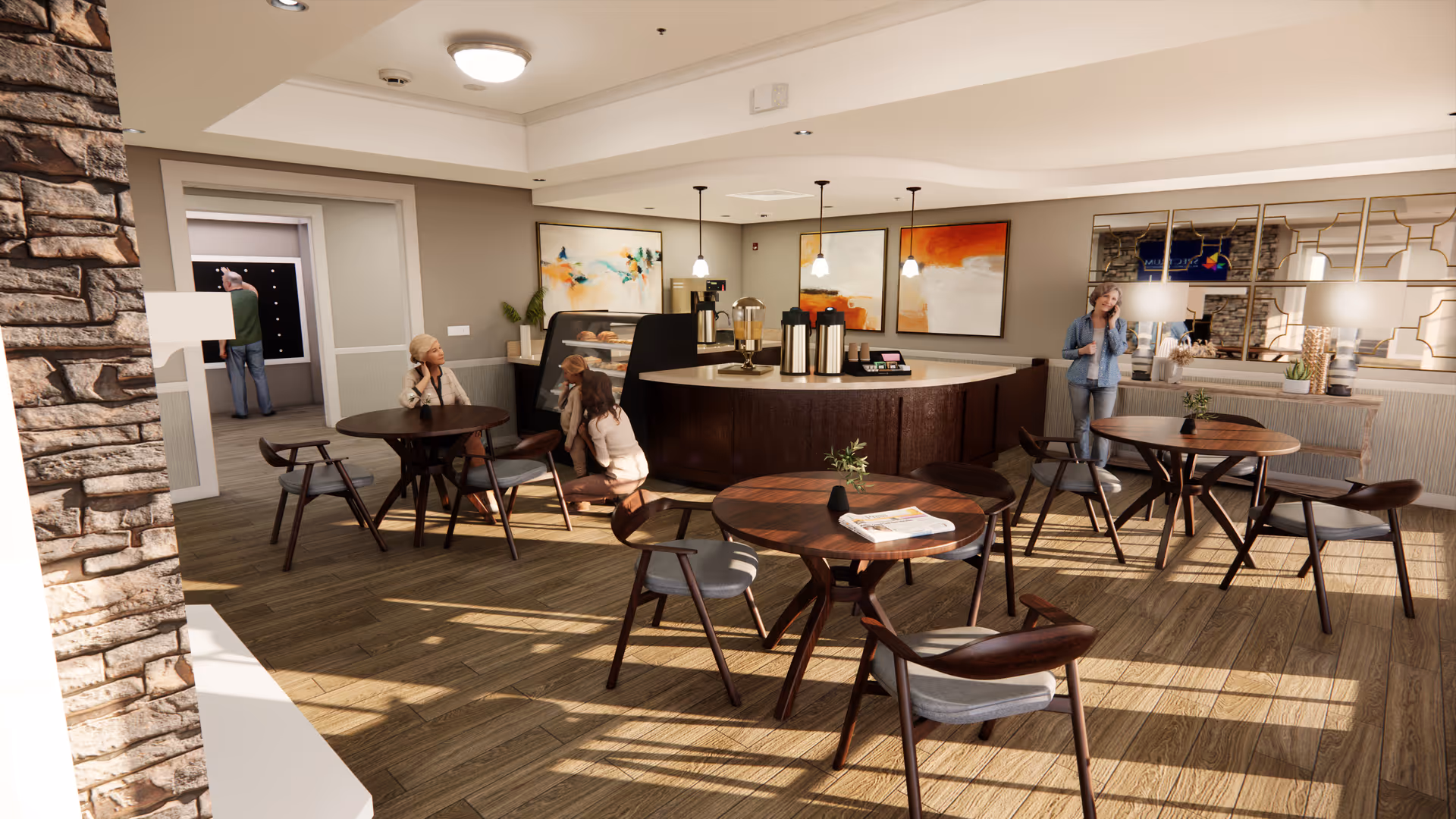 A bright and modern dining area in a senior living facility with round wooden tables and chairs. There are three people in the room: one elderly woman sitting at a table, another elderly woman crouching near a display case with pastries, and a younger woman standing near the counter talking on the phone. The room features wood flooring, pendant lights, abstract artwork on the walls, and a stone accent wall on the left side.