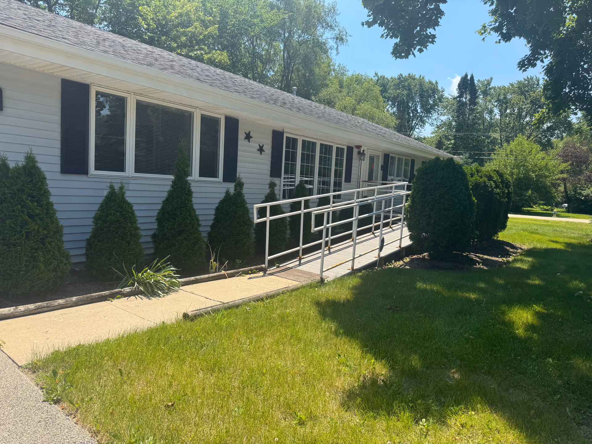 White, single-story building with a metal ramp, shrubbery, and a well-kept front lawn.