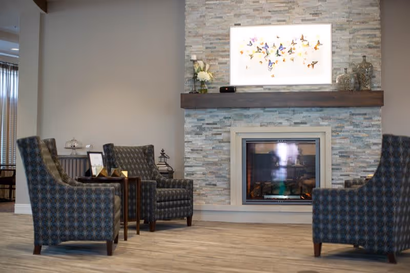 Cozy seating area with patterned armchairs arranged around a modern stone fireplace and mantel artwork.