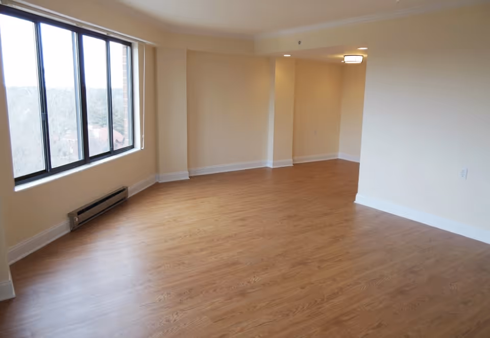 Empty bright living room with large windows and wood laminate flooring.