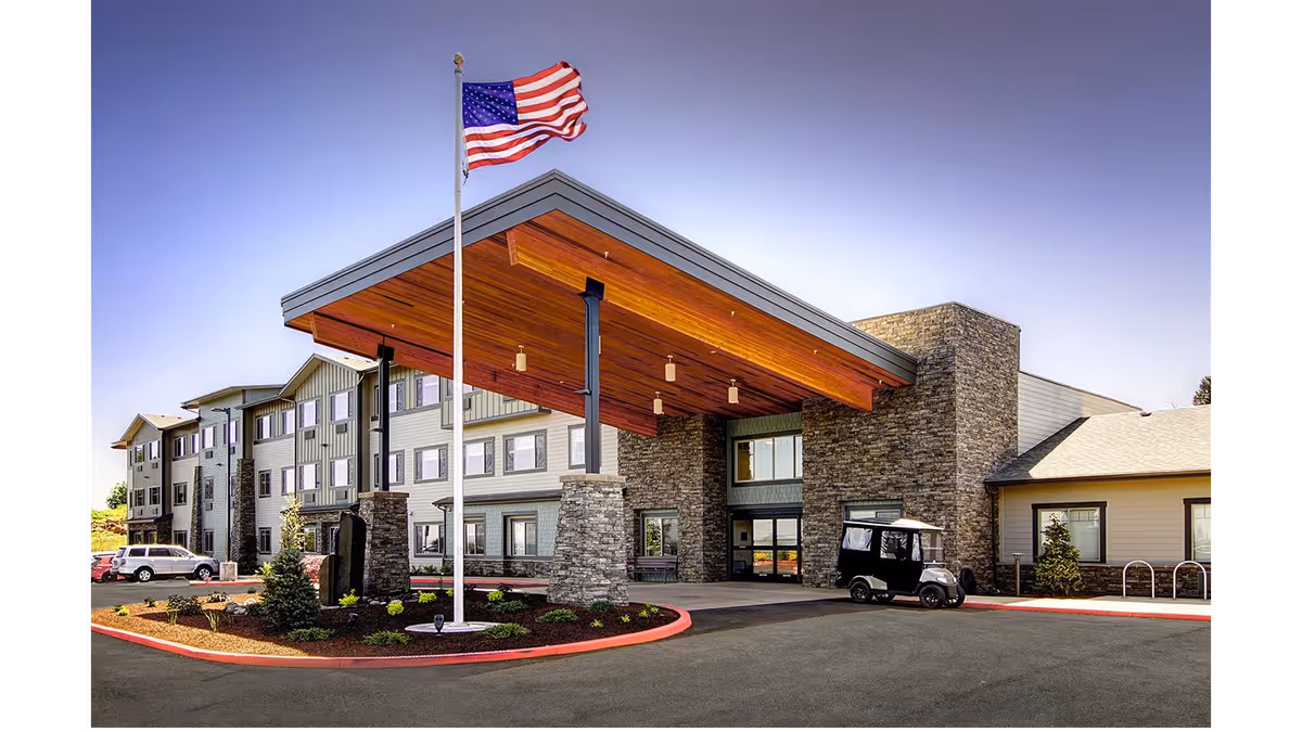 Entrance canopy and driveway of a multi-story senior living building with an American flag and a small cart parked by the covered entry.