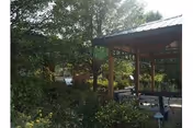 Wooden gazebo with picnic tables surrounded by trees, shrubs, and landscaping in an outdoor courtyard.