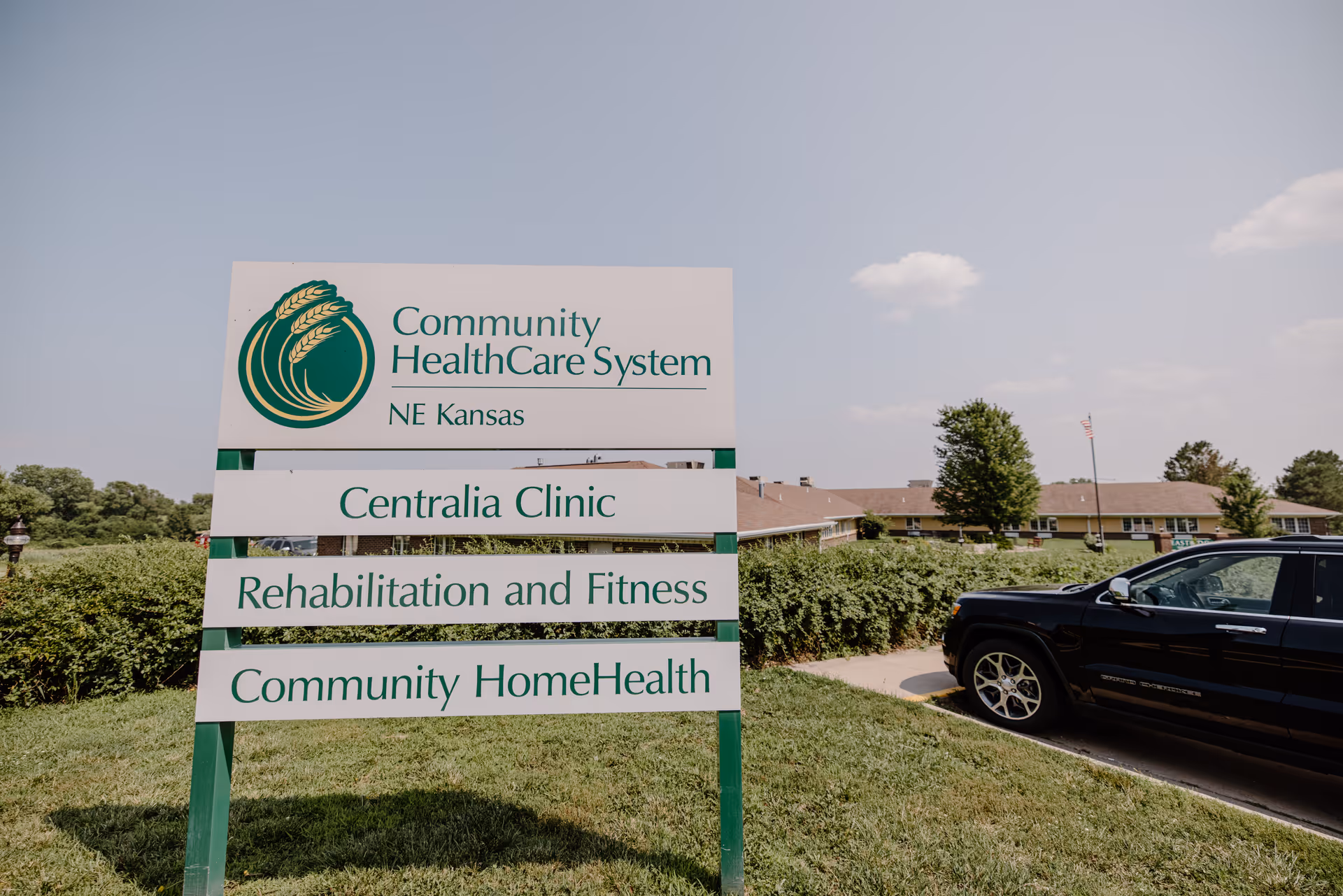 Outdoor sign for Community HealthCare System NE Kansas listing Centralia Clinic, Rehabilitation and Fitness, and Community HomeHealth with the facility building and a parked car in the background.