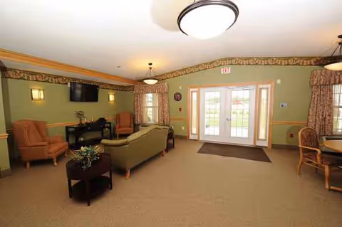 Senior living lobby with seating area, coffee tables, mounted TV, and glass entry doors.
