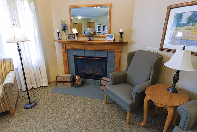 Cozy living room corner with a fireplace, mantel mirror, armchairs, side table, and floor lamp.