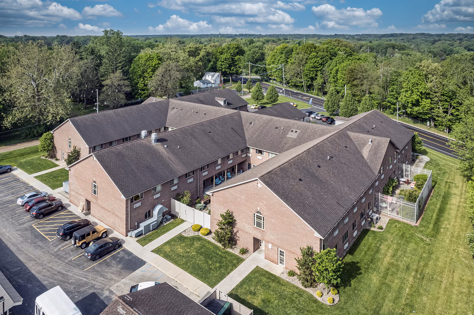 Aerial view of a brick senior living complex with multiple connected buildings, parking spaces, lawns, and surrounding trees.