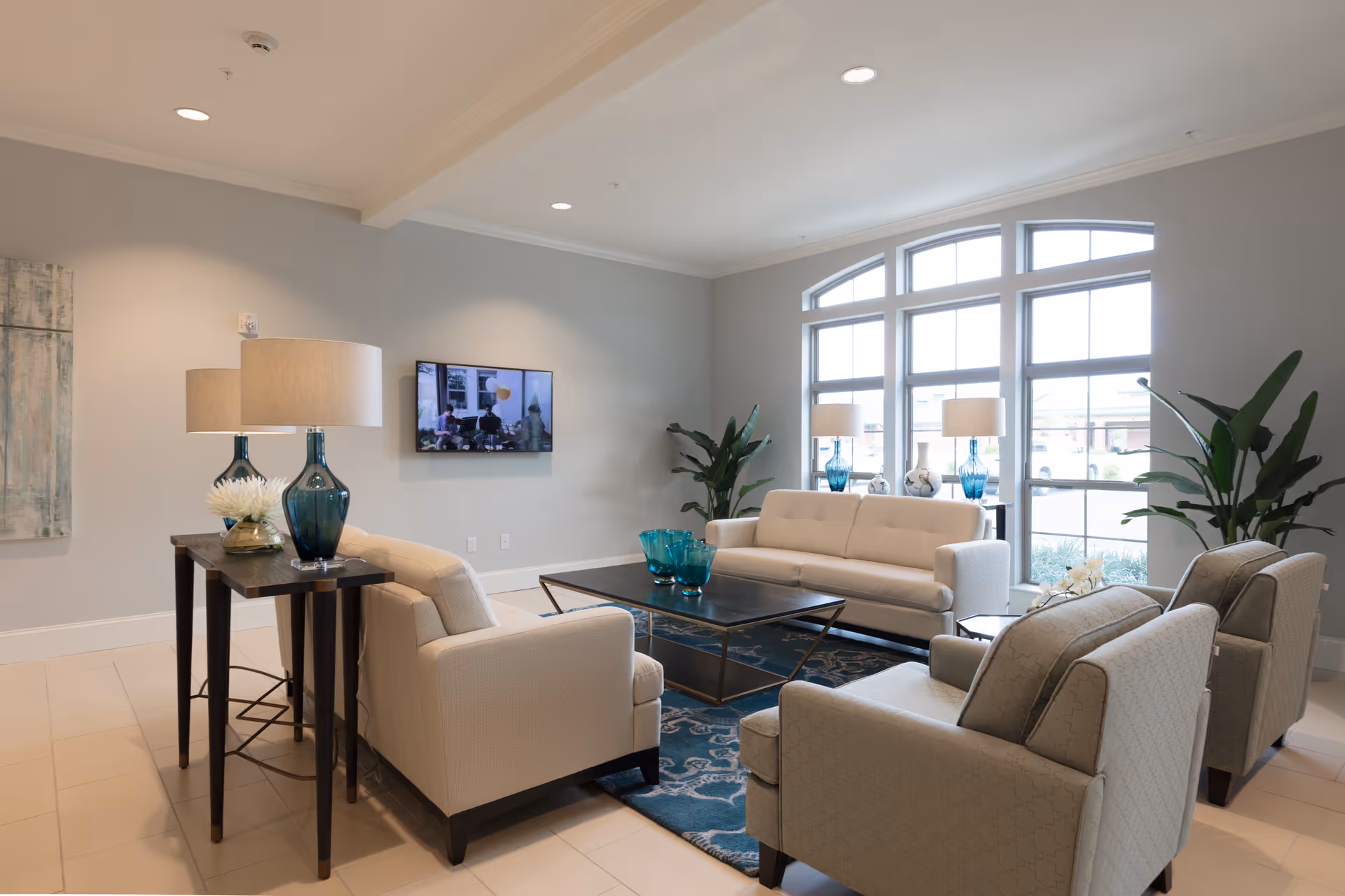 Bright, modern lounge with sofas, armchairs, a coffee table, decorative lamps and large arched windows.