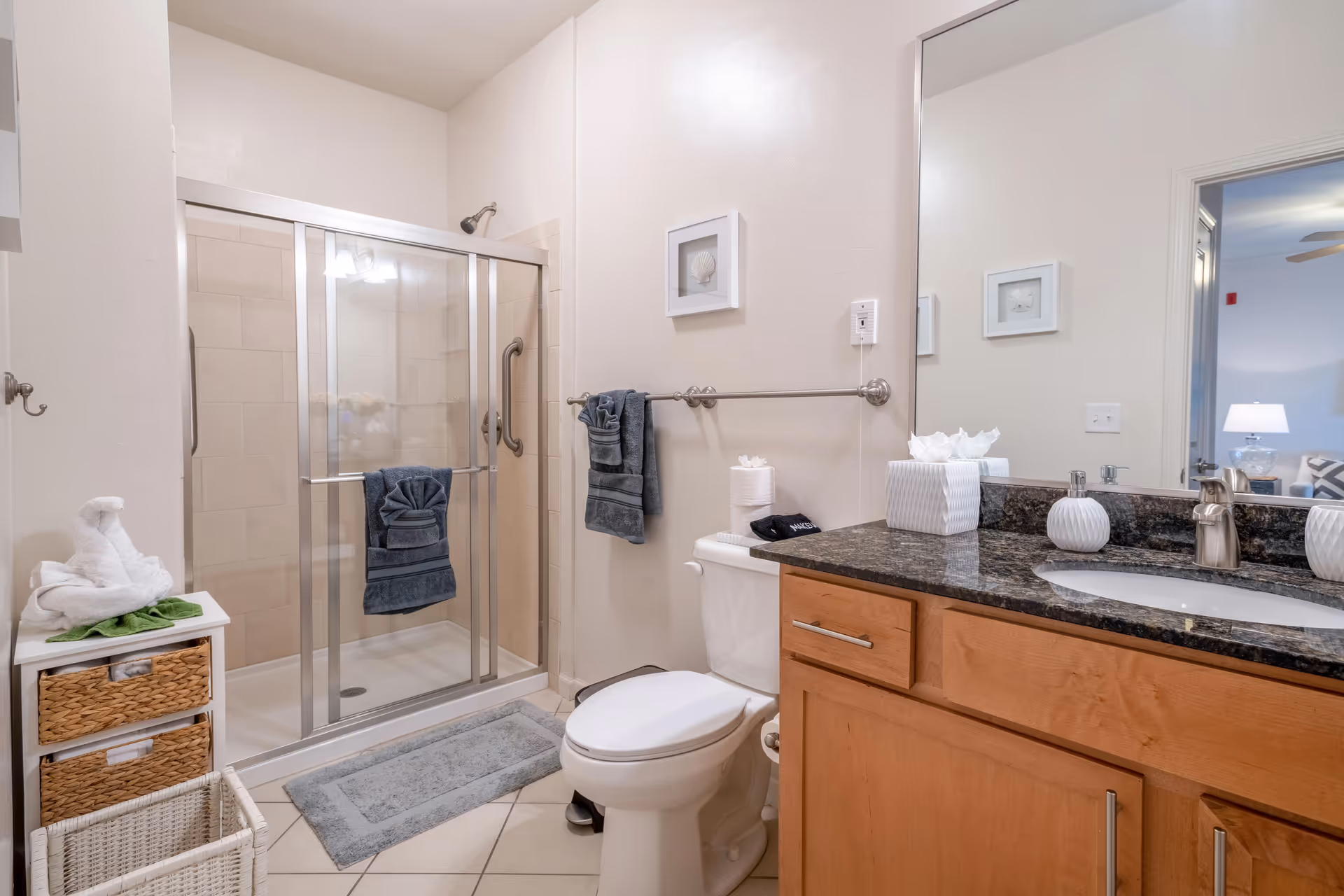 A clean bathroom with a glass-enclosed shower, toilet, and a granite-top vanity with mirror.
