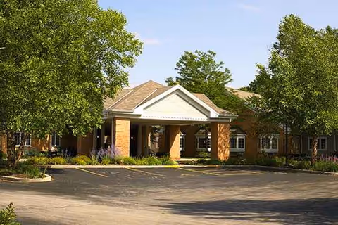 Senior living facility entrance with porte-cochere, brick facade, and surrounding trees.
