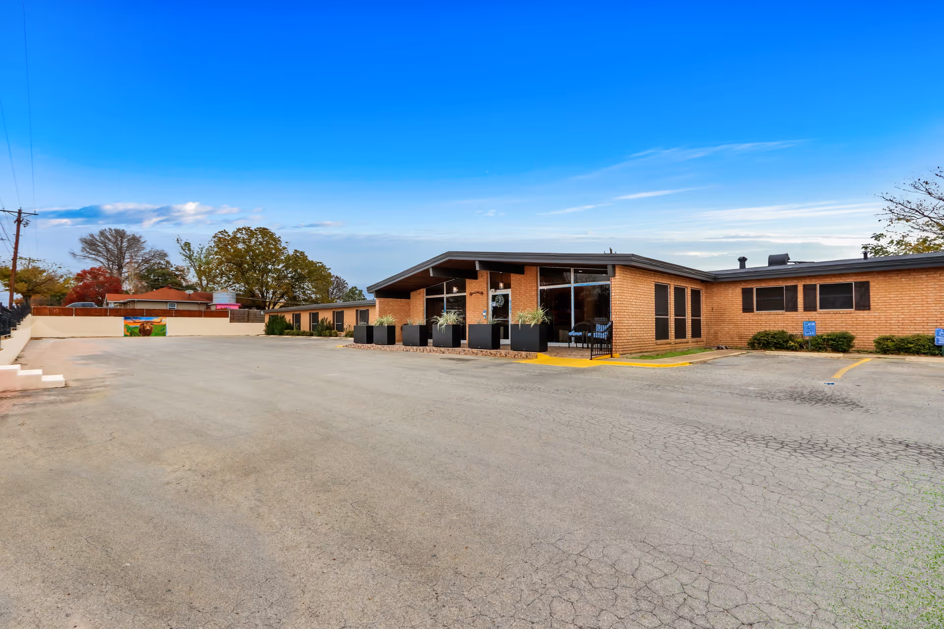 Single-story brick nursing facility front with a wide empty parking lot and clear blue sky.