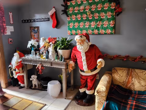 A cozy sitting area decorated for Christmas with life-size Santa figures, a console table with plants and holiday ornaments, and a couch with a blanket.