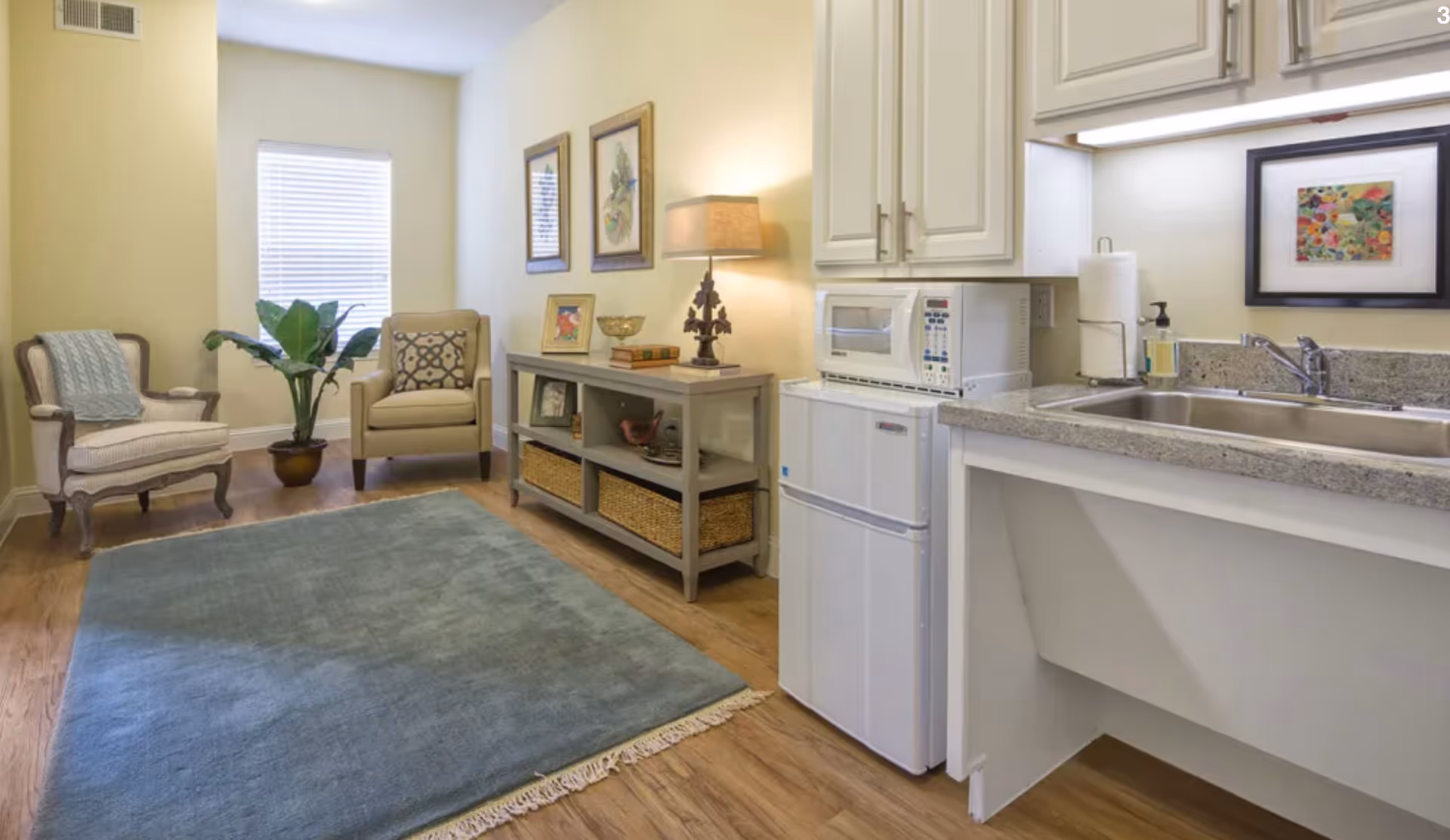 Small studio living area with two chairs, a console table, area rug and a kitchenette with sink and mini fridge.