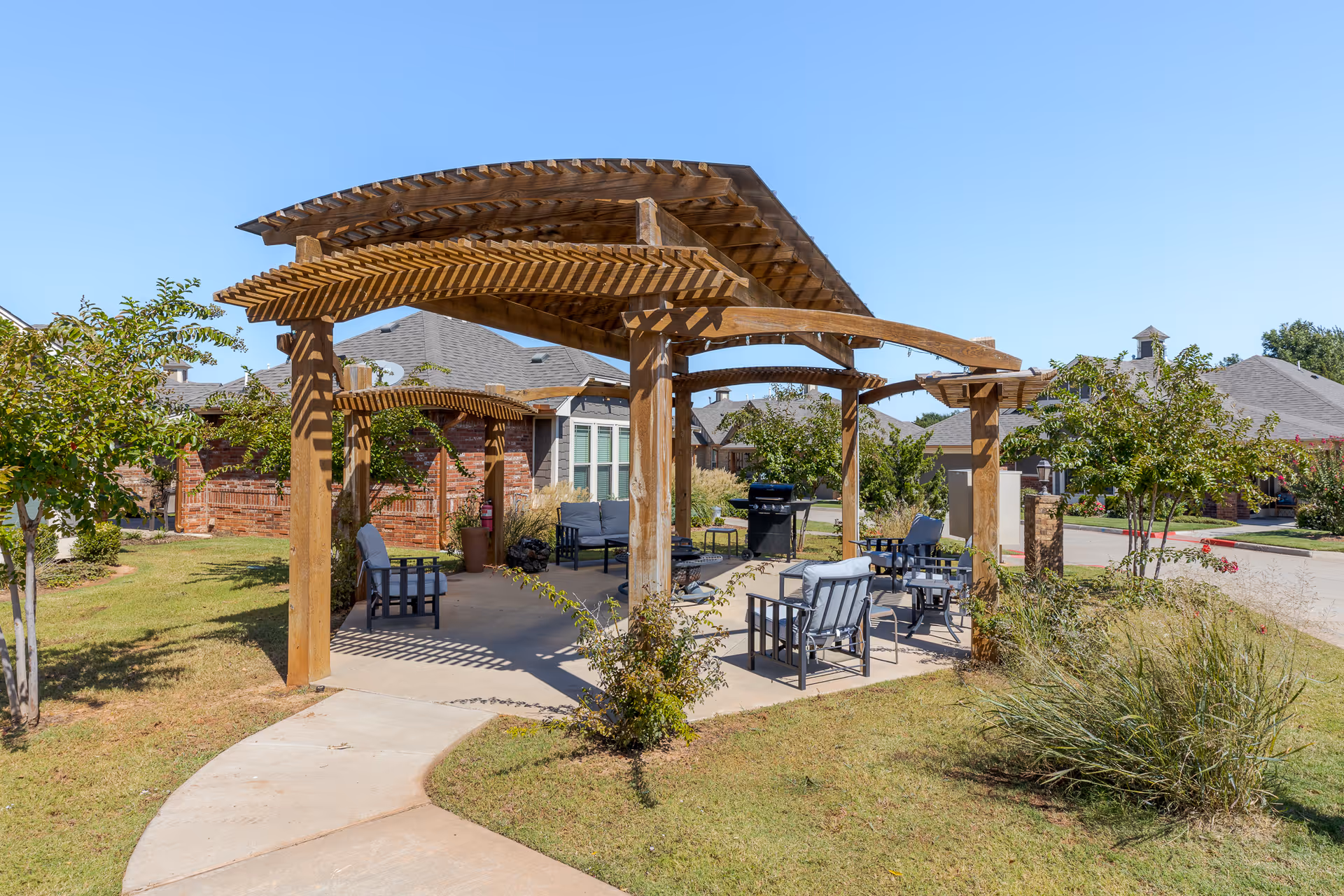 Wooden pergola covering patio chairs and a grill in a landscaped outdoor seating area.