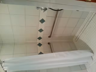 Tiled walk-in shower with a white curtain, wall-mounted grab bars, and a showerhead.