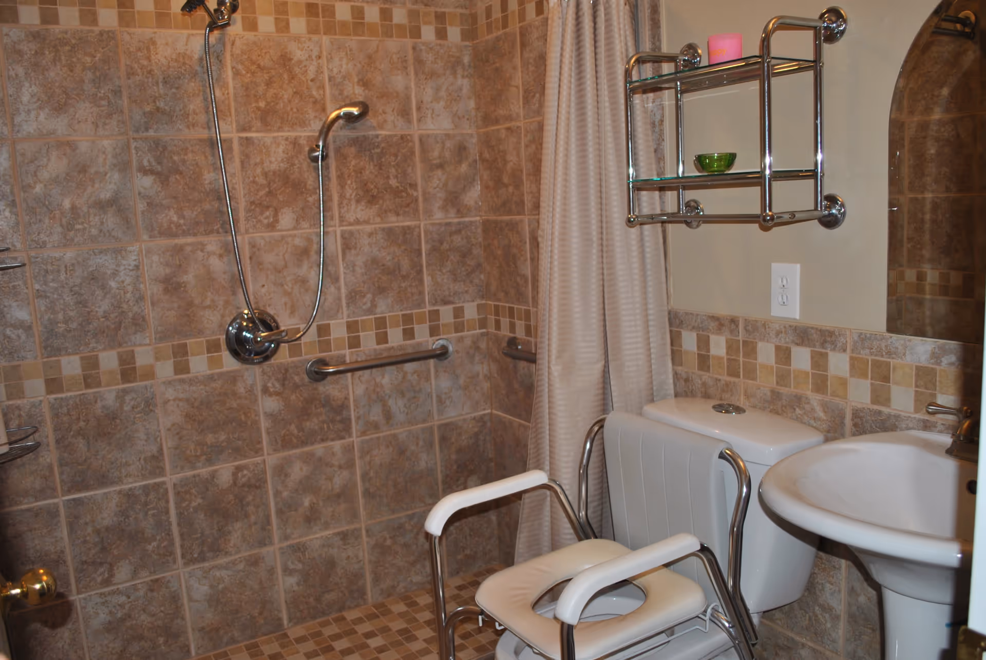Accessible bathroom with tiled walk-in shower, grab bars, shower chair, toilet and sink.