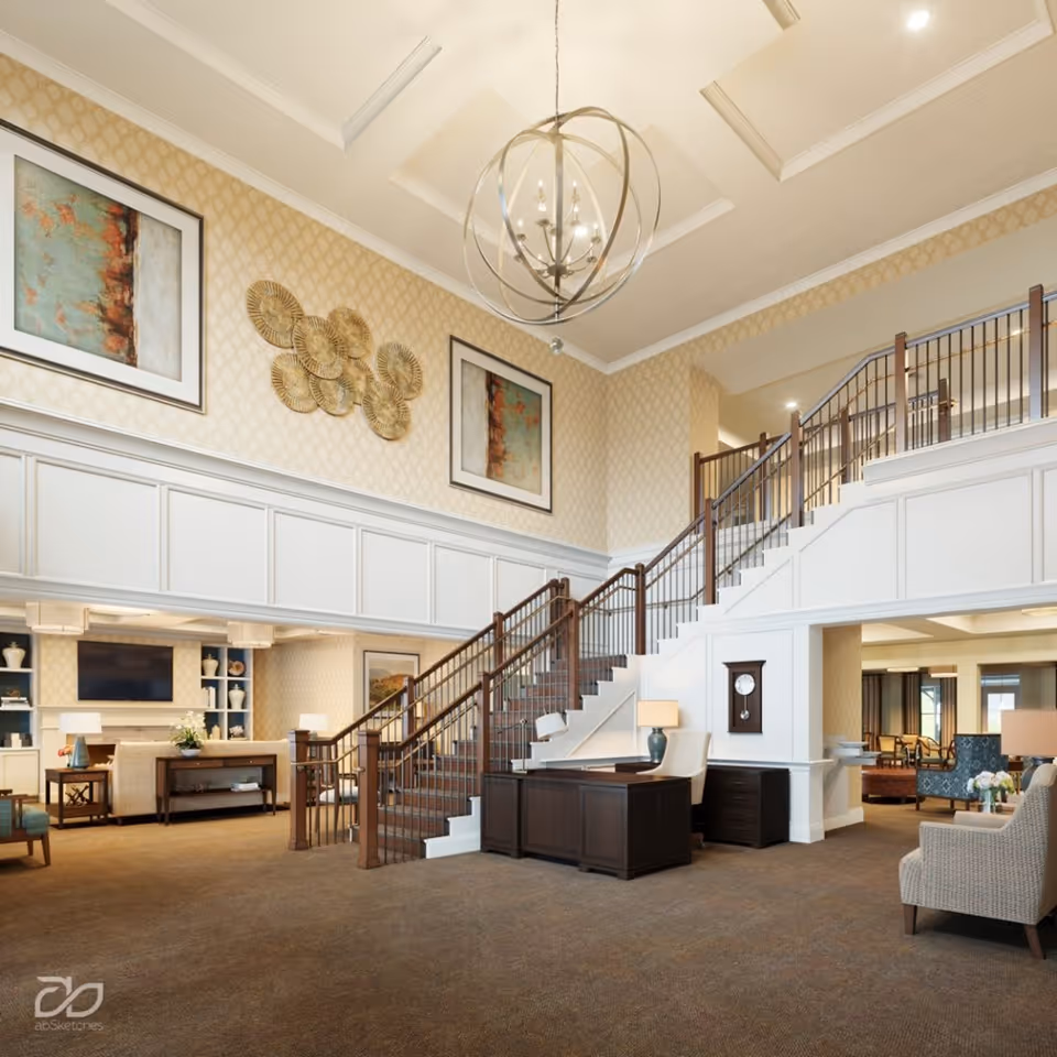 Spacious and elegant interior of a senior living facility featuring a large staircase with wooden railings, a chandelier hanging from a coffered ceiling, patterned wallpaper, framed artwork, and comfortable seating areas with chairs and tables.