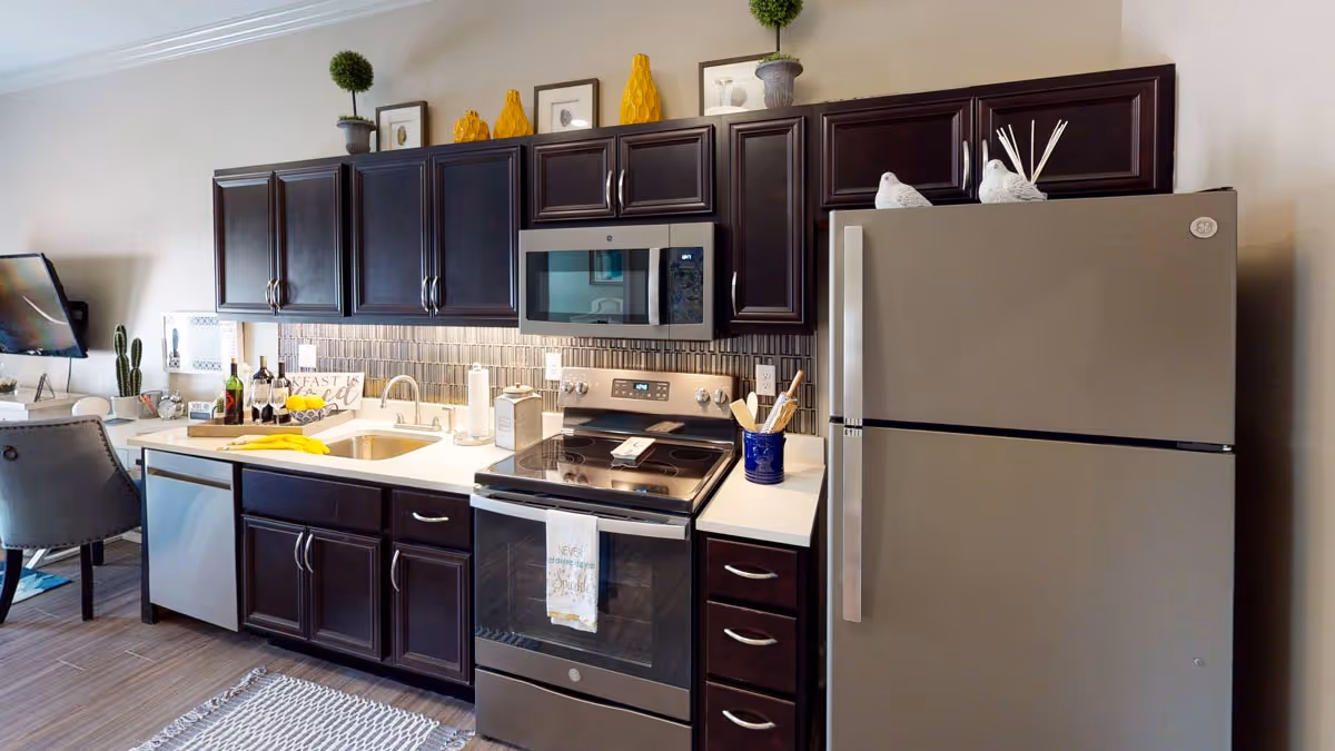 Open-concept kitchen with dark wood cabinets, a stainless steel refrigerator, stove and microwave, sink and decorated countertops.