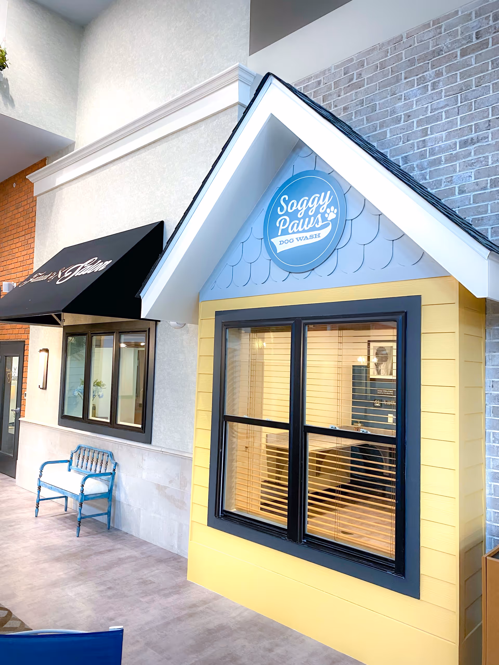 Interior hallway showing a small yellow mock storefront labeled "Soggy Paws Dog Wash" with a window and a blue bench nearby.