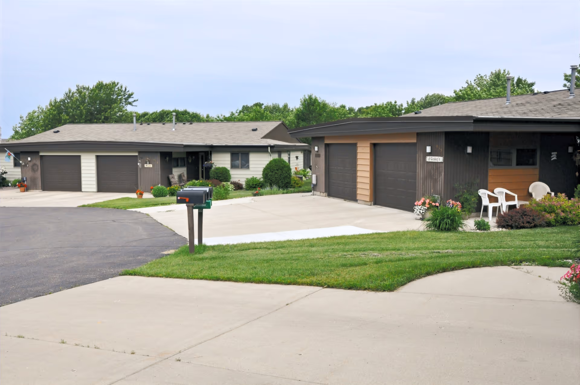 Single-story retirement village buildings with attached garages, driveways, a mailbox, and manicured lawns.