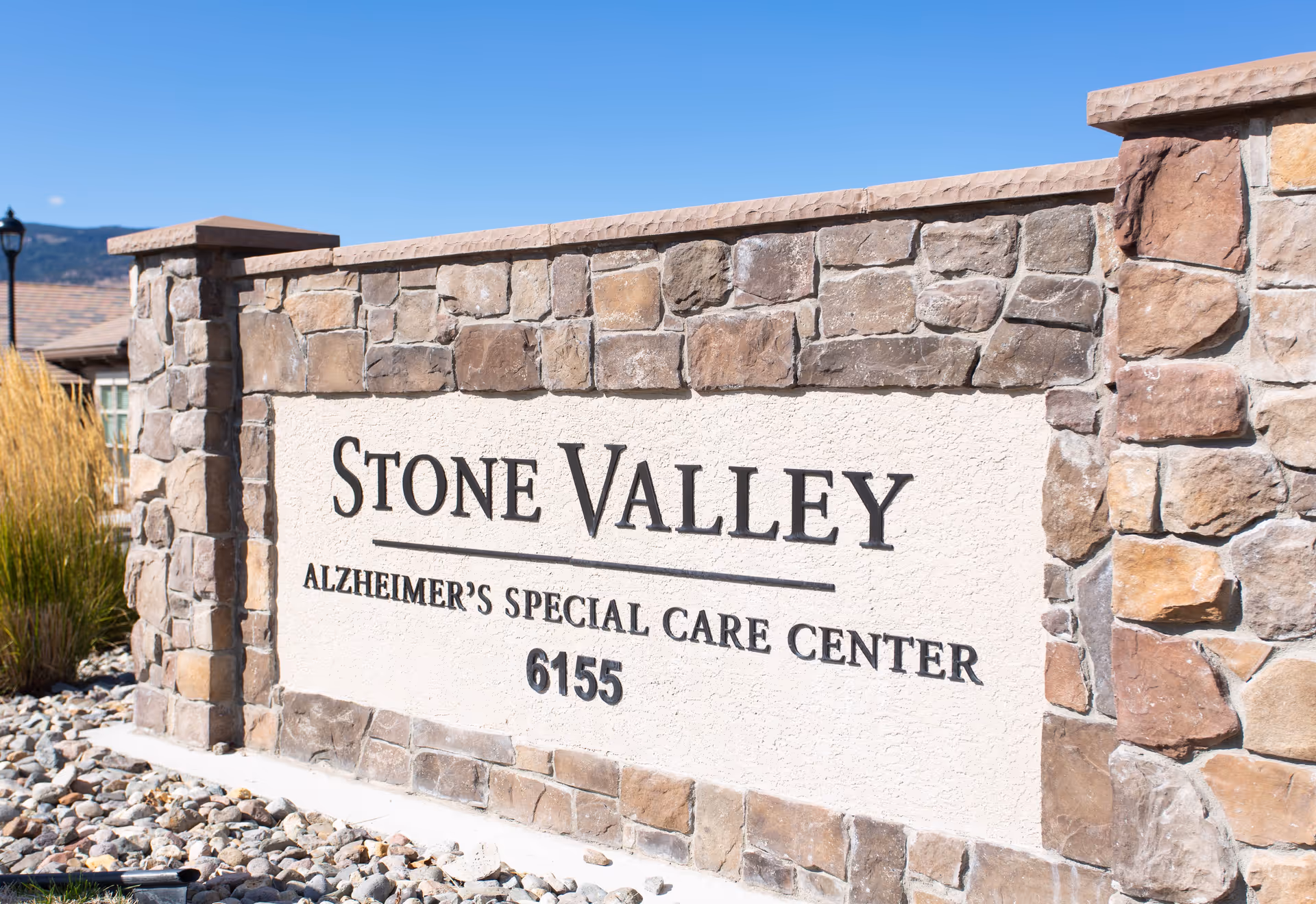 Stone Valley Alzheimer's Special Care Center sign made of stone and stucco with the number 6155, set outdoors with clear blue sky and some landscaping visible.
