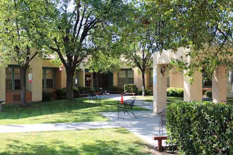 Outdoor courtyard with trees, benches, and seating around a beige senior living building