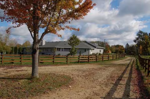Single-story care facility exterior with wooden fence, dirt path, and autumn trees.