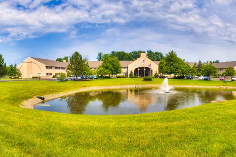 Exterior view of The Abbewood facility with a pond, fountain, and manicured lawn.