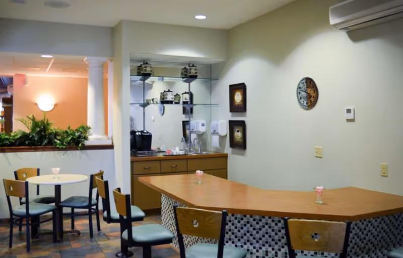Community dining area with round tables and chairs, a curved service counter with tiled front, and a coffee station against the back wall.