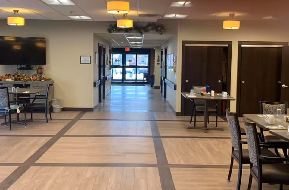 Spacious assisted living dining area with tables and chairs leading to a hallway and entrance.