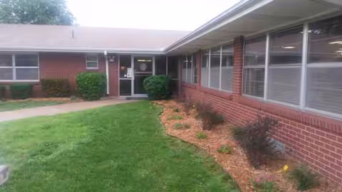 Front exterior view of Medicalodges Arkansas City facility: brick building, windows, entrance, and landscaping.
