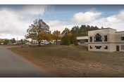 Exterior view of a senior living facility named Elderwood at North Creek, showing a two-story building on the right and several smaller buildings surrounded by trees with autumn foliage under a partly cloudy sky.