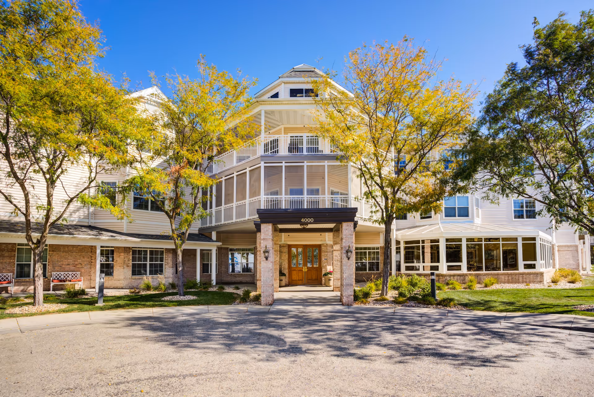 Front exterior view of The Inn on Westport building with a covered entrance, surrounded by trees with yellow and green leaves under a clear blue sky.