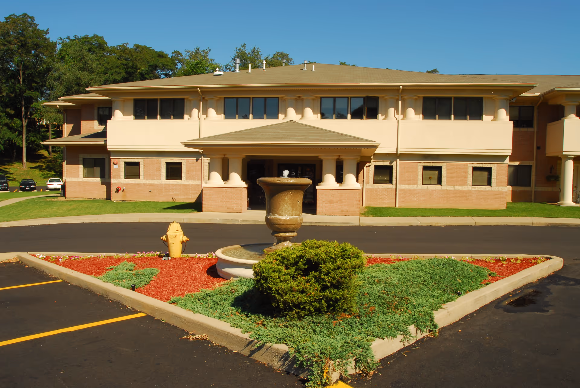 Senior living facility exterior with a central fountain and landscaped island.