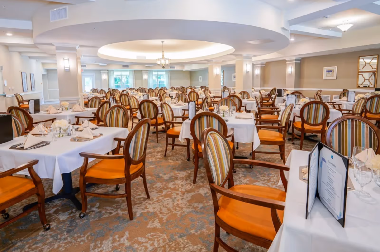 Large elegant dining room with numerous tables set with white tablecloths and striped-back wooden chairs.