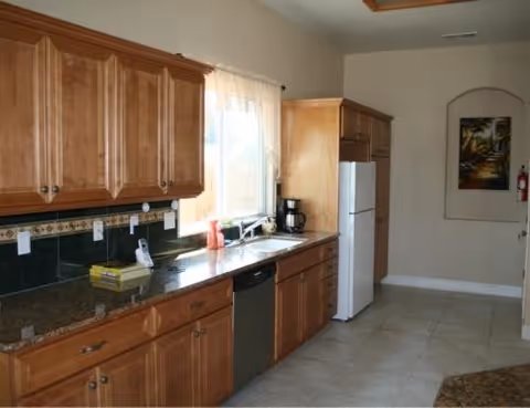 Bright wooden kitchen with countertops, sink, dishwasher, refrigerator, window, and coffee maker.
