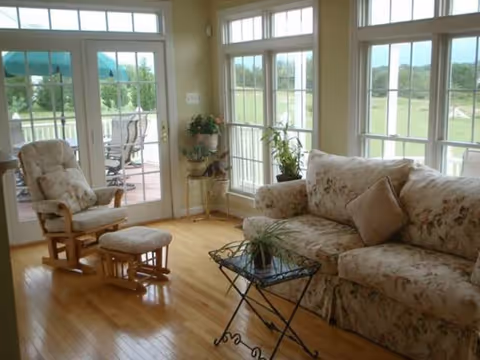Sunlit living room with floral sofa, rocking chair, glass table, and patio doors.