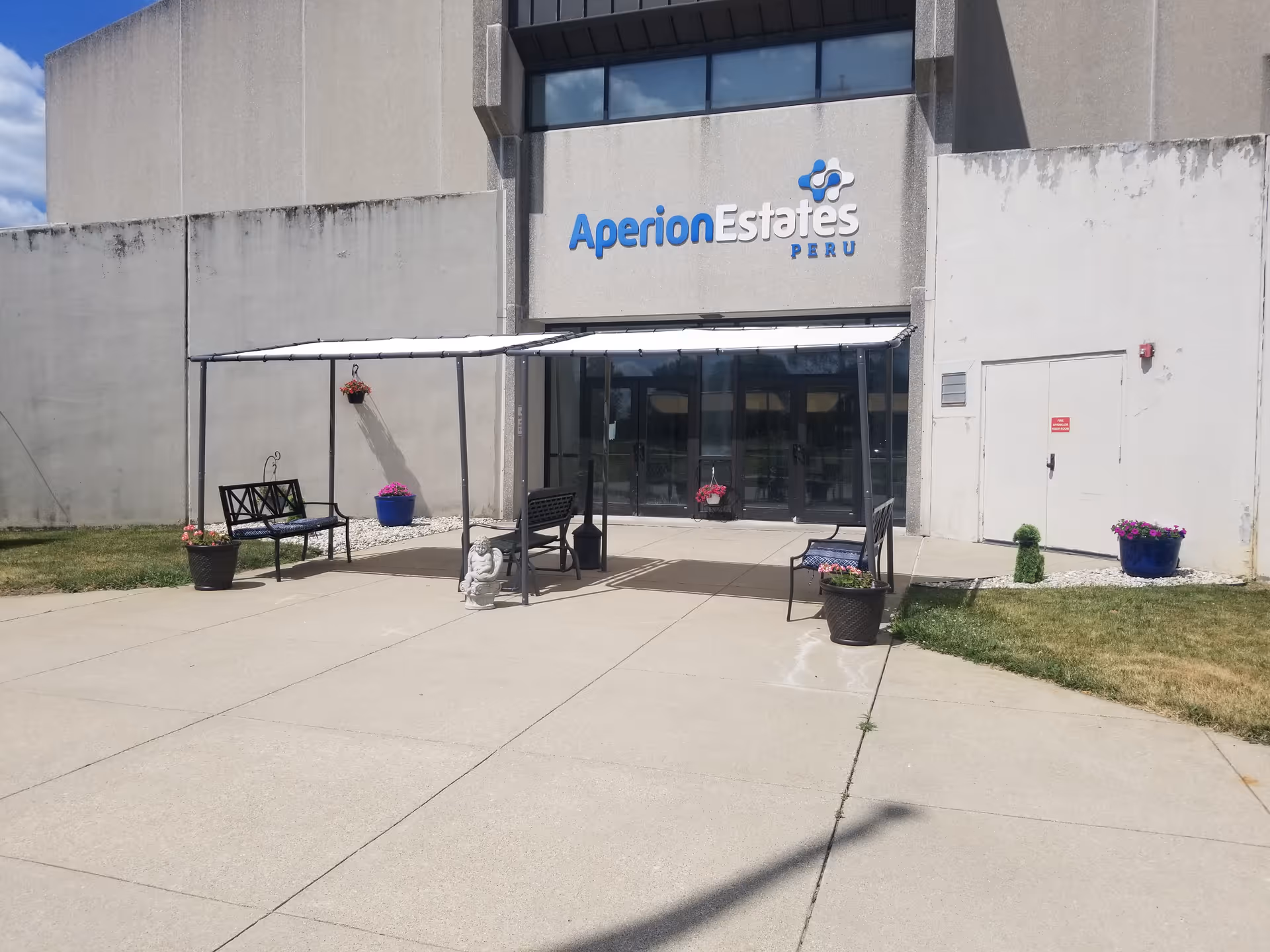 Front entrance of Aperion Estates Peru with a canopy, benches, potted plants, and the facility sign above the glass doors.