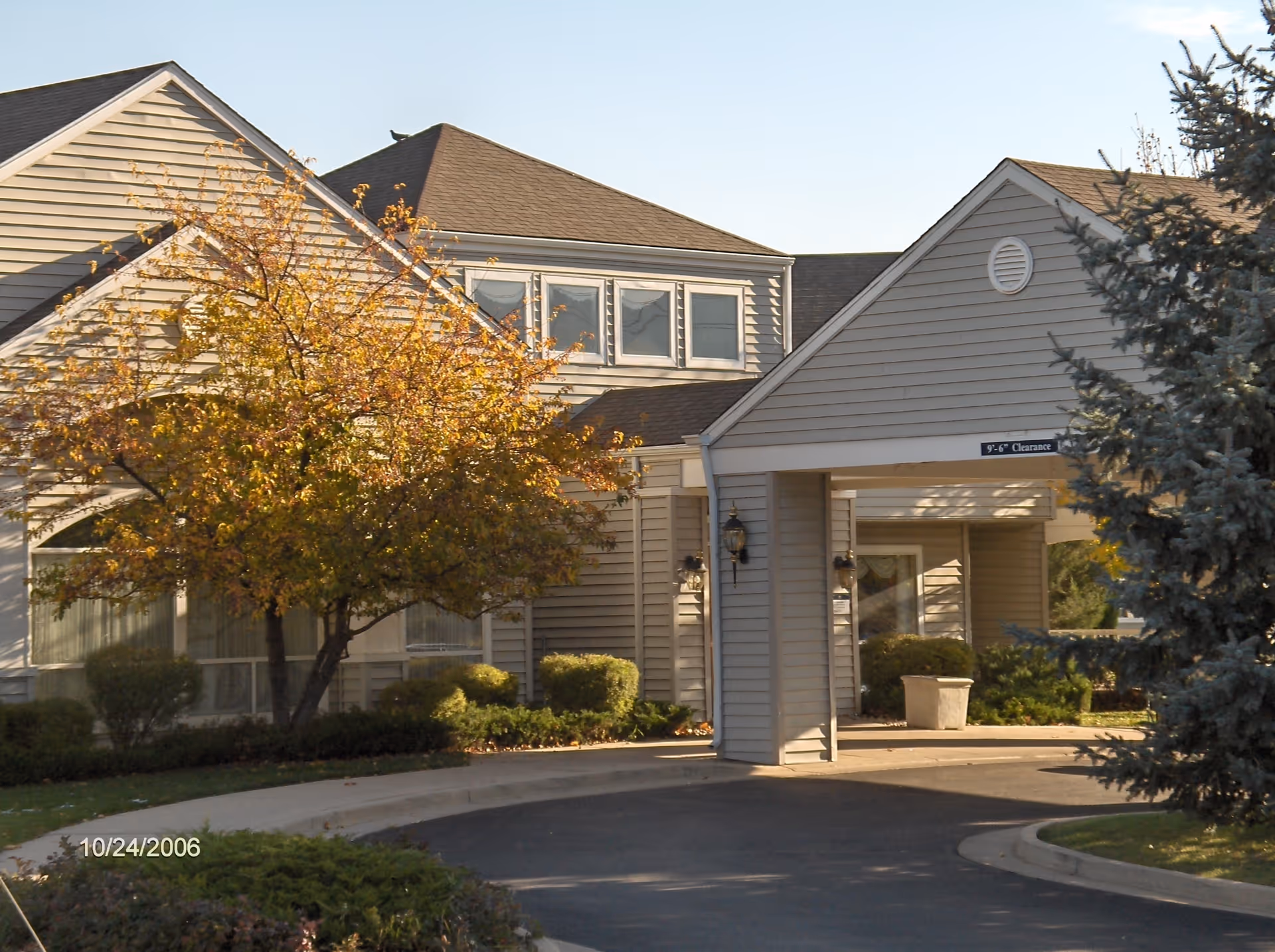 Front entrance and porte-cochère of a senior living building with autumn trees and a curved driveway.