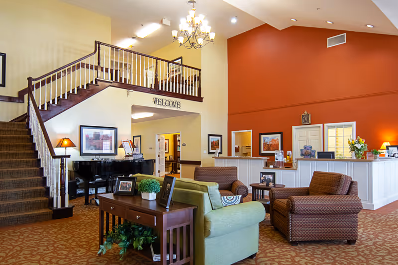 Spacious assisted living facility lobby with seating area, reception desk, staircase and piano.