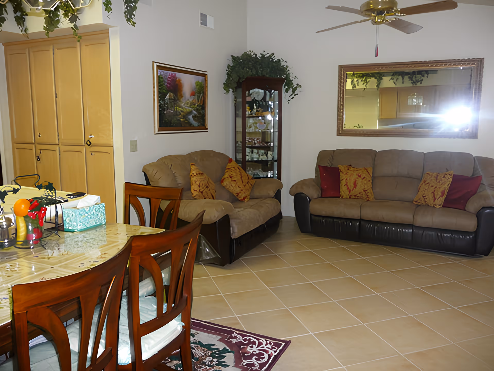 Open living and dining area with a sofa set, wooden dining table and chairs, wall mirror, and glass display cabinet.