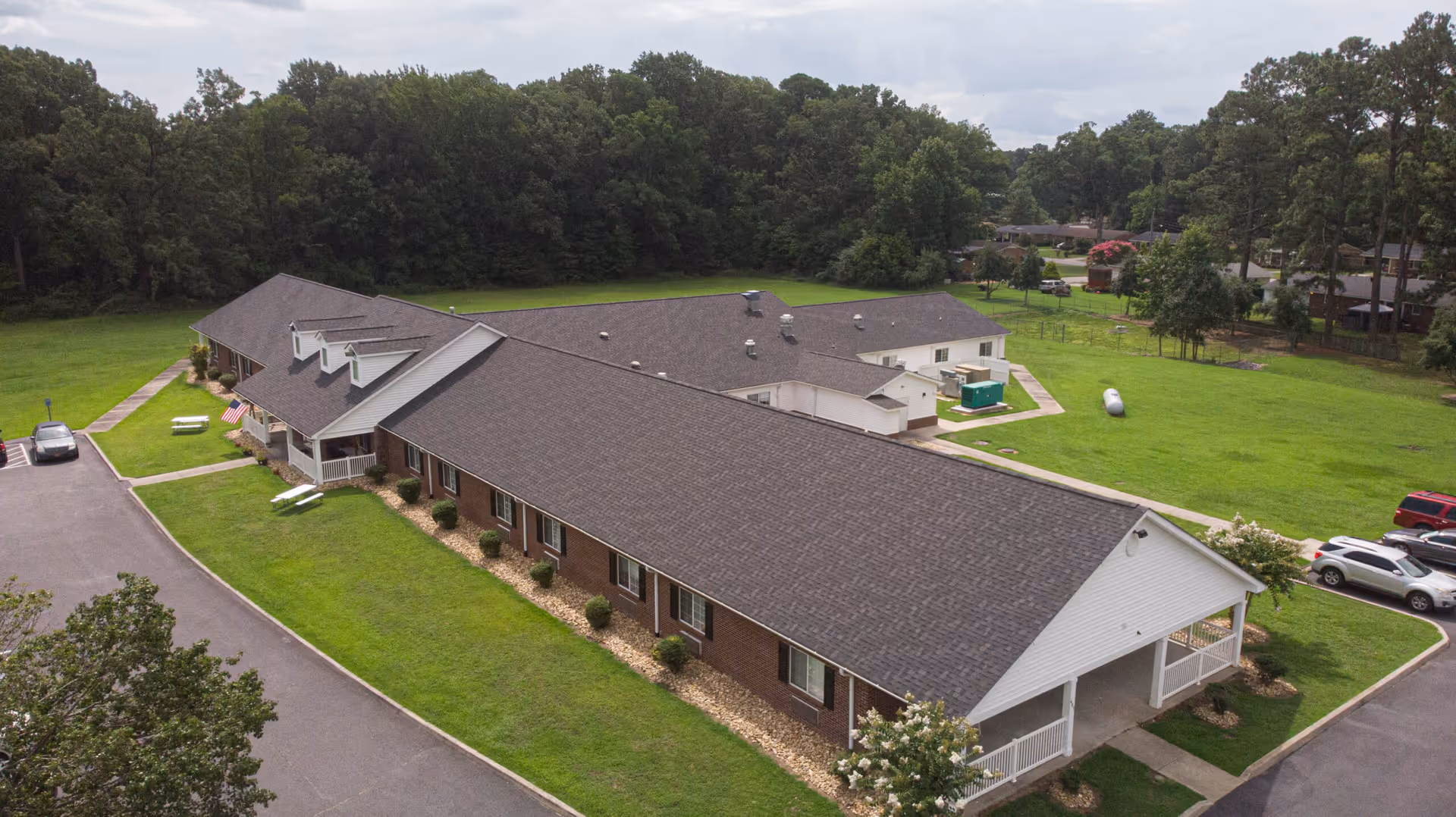 Aerial view of a single-story senior living facility named Ahoskie House surrounded by green lawns and trees, with a parking area and several cars visible.